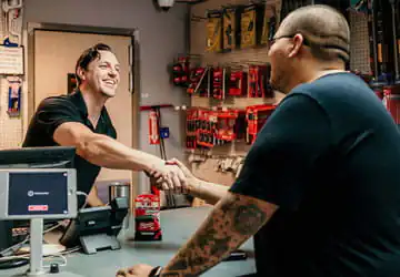 Smiling employee at a plumbing service counter shaking hands with a contractor